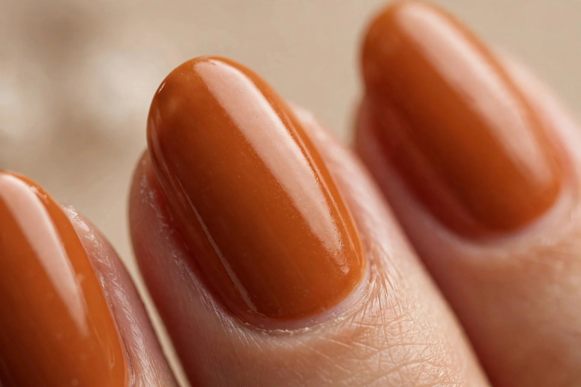Medium almond nails in pumpkin-orange-brown creme polish, glossy, beige background