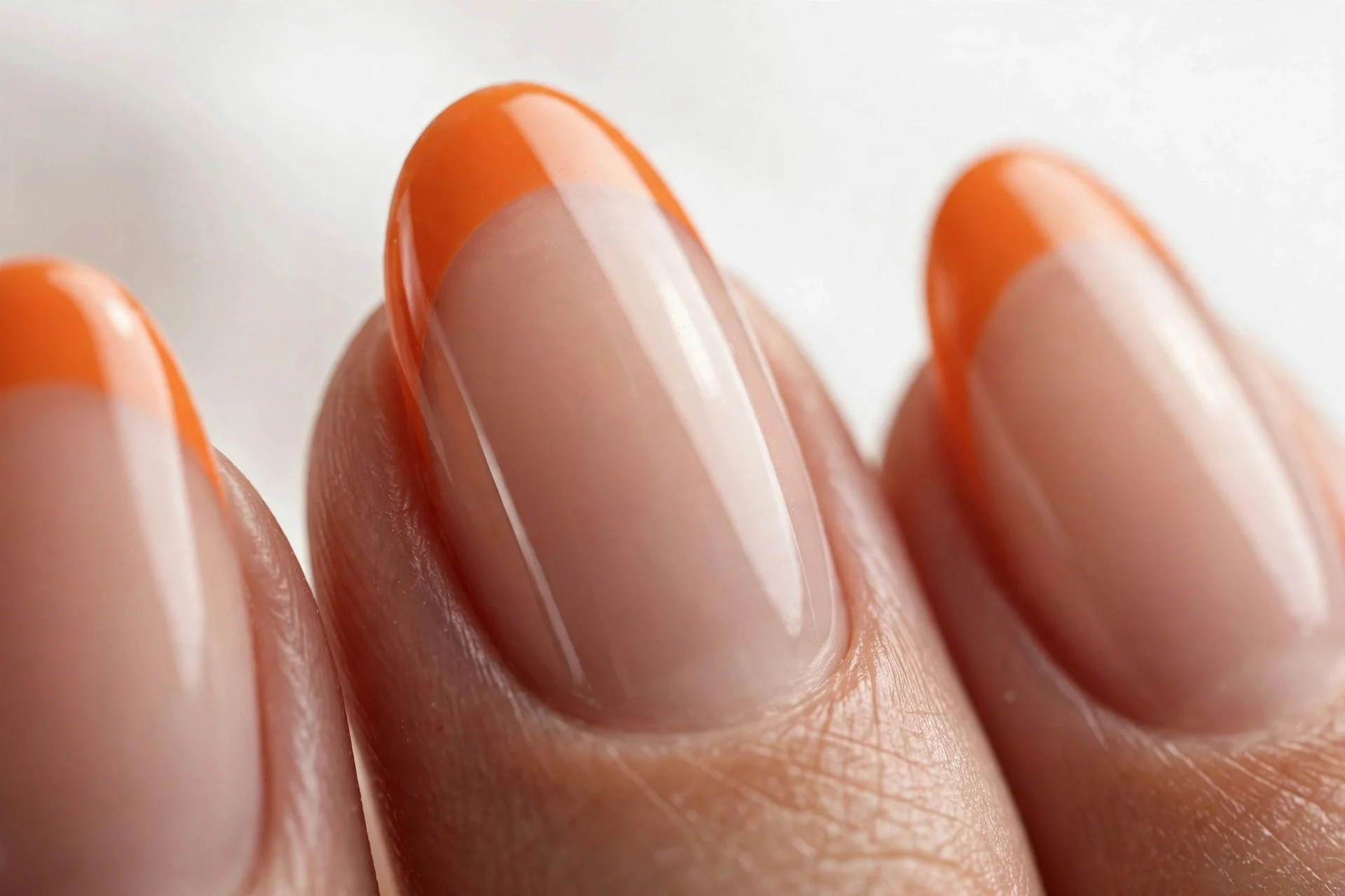 Almond nails with sheer nude base and pumpkin-orange French tips, glossy, white background