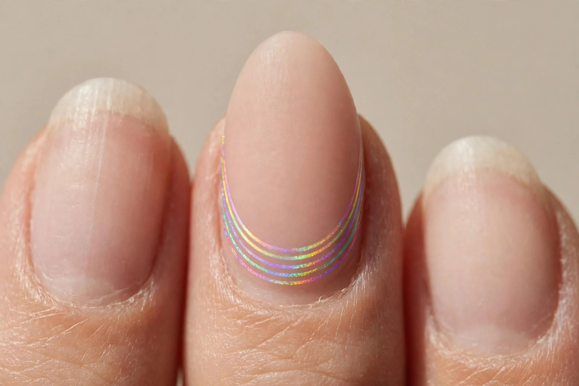 one almond fingernail with rainbow bands along the smile line over a nude nail bed