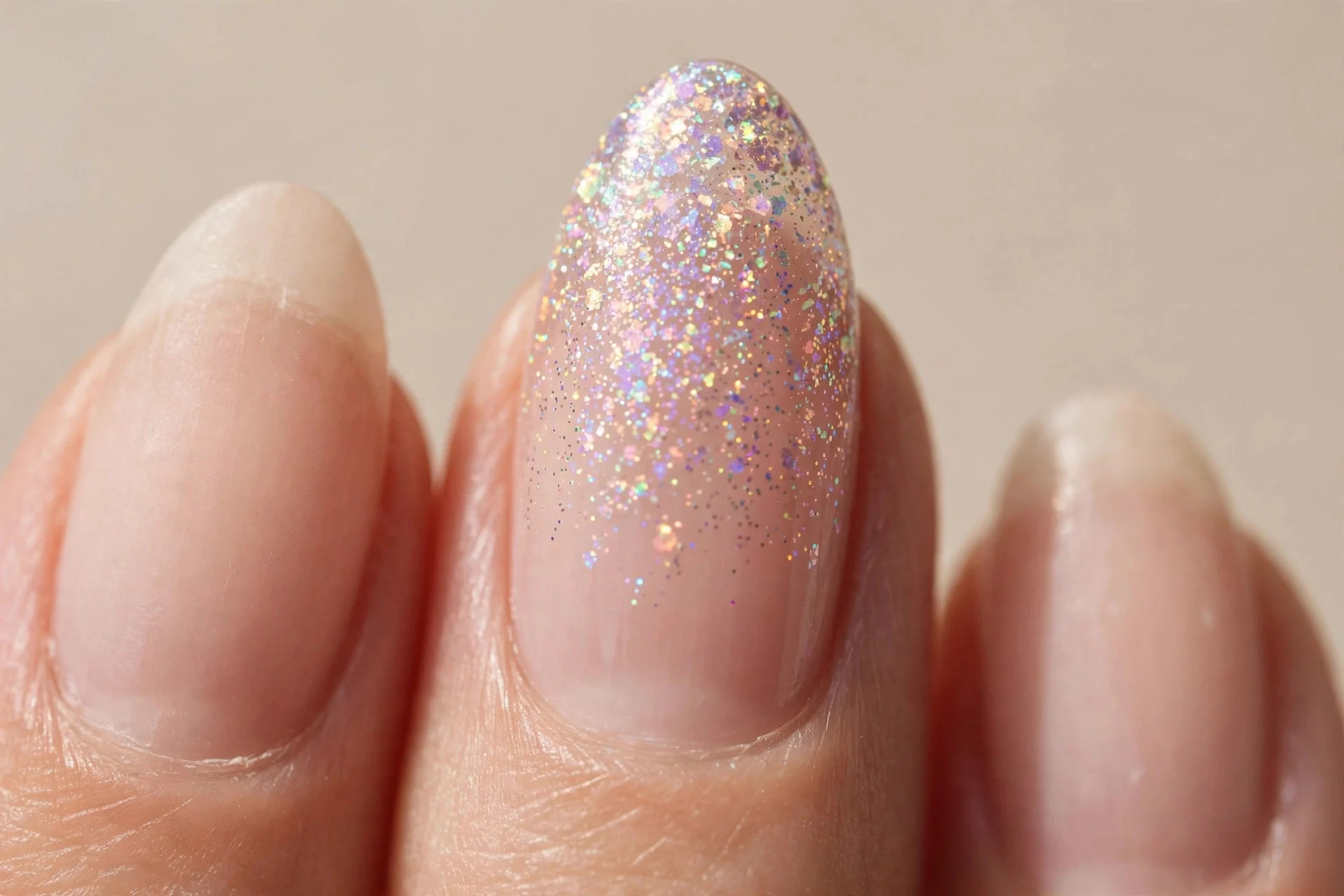 one almond fingernail with holographic glitter fading from the tip into a sheer nude base