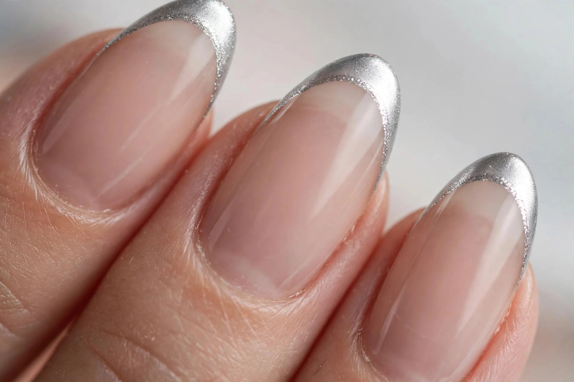 Sheer nude nails with bright silver French tips, almond nails