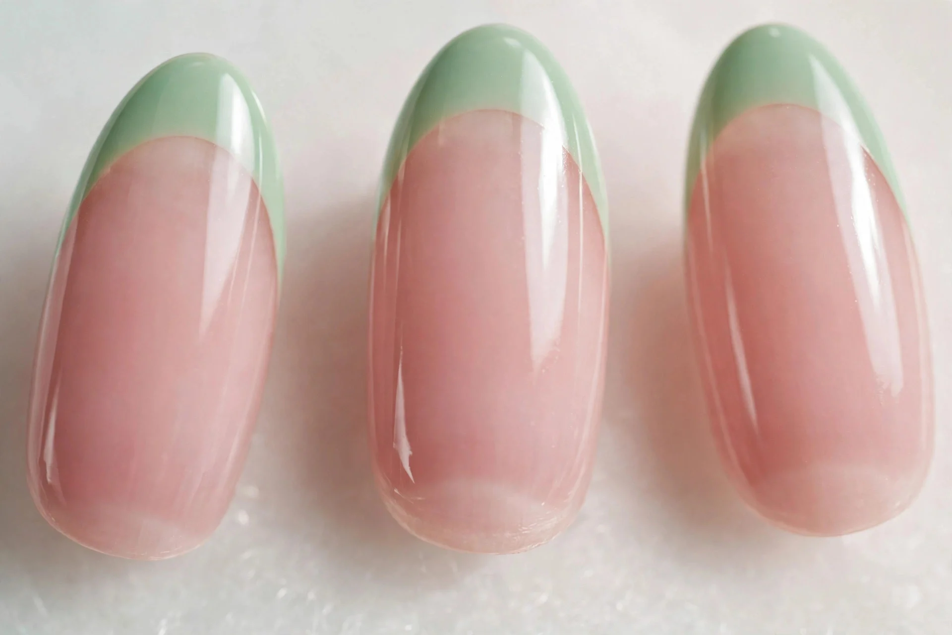 Almond nails with mint green French tips on sheer pink base, glossy, light background