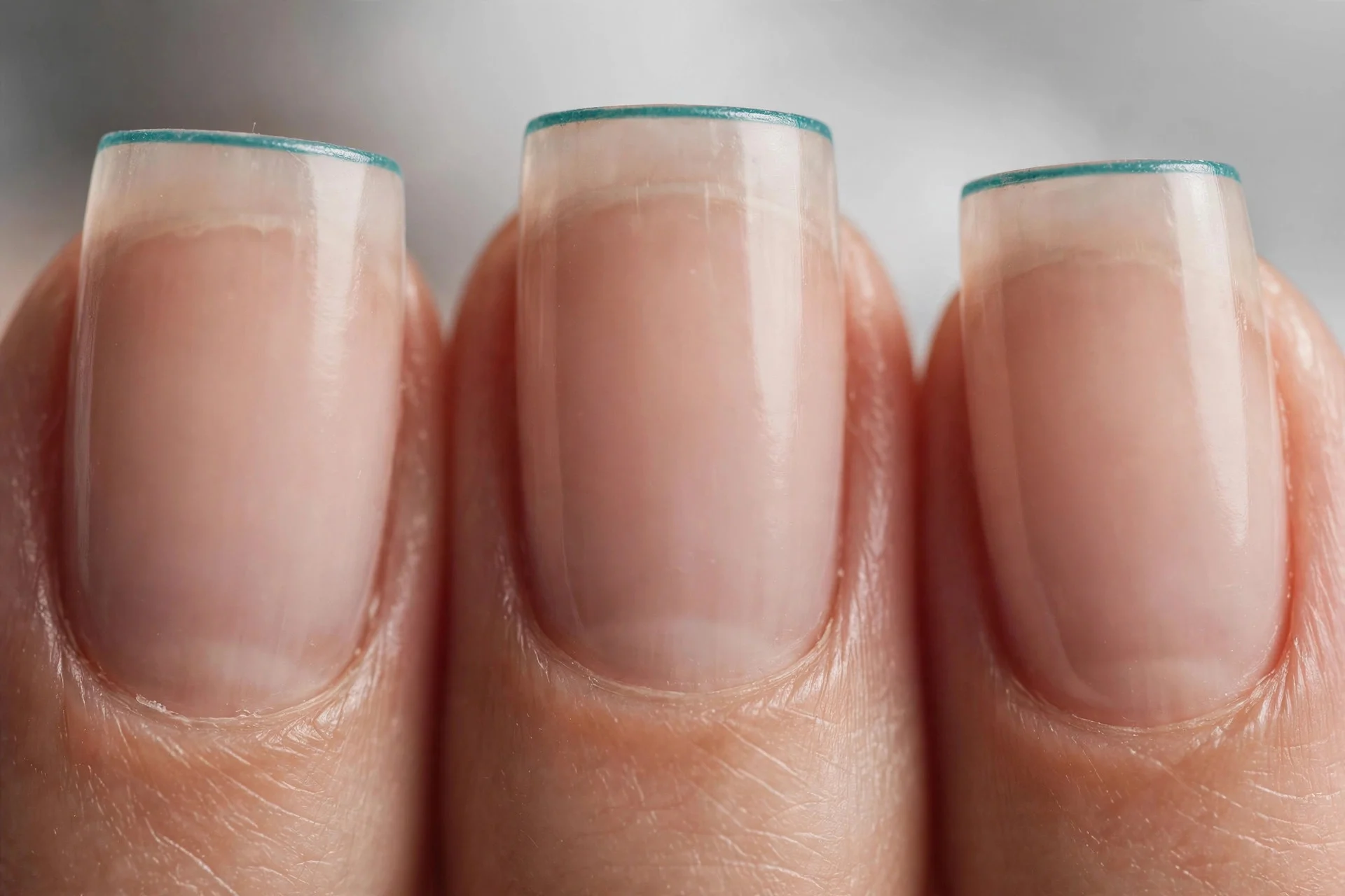 Sheer nude nails with thin teal micro French tips, square