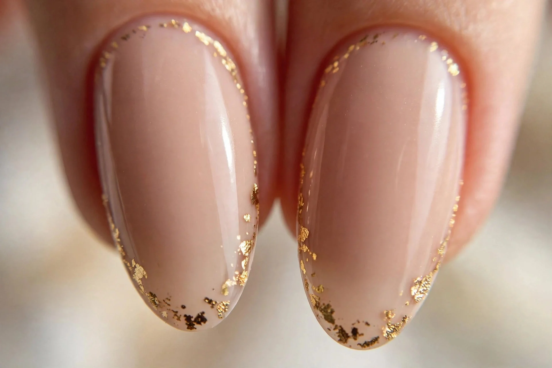two almond fingernails in nude polish with tiny gold foil flecks along the edge