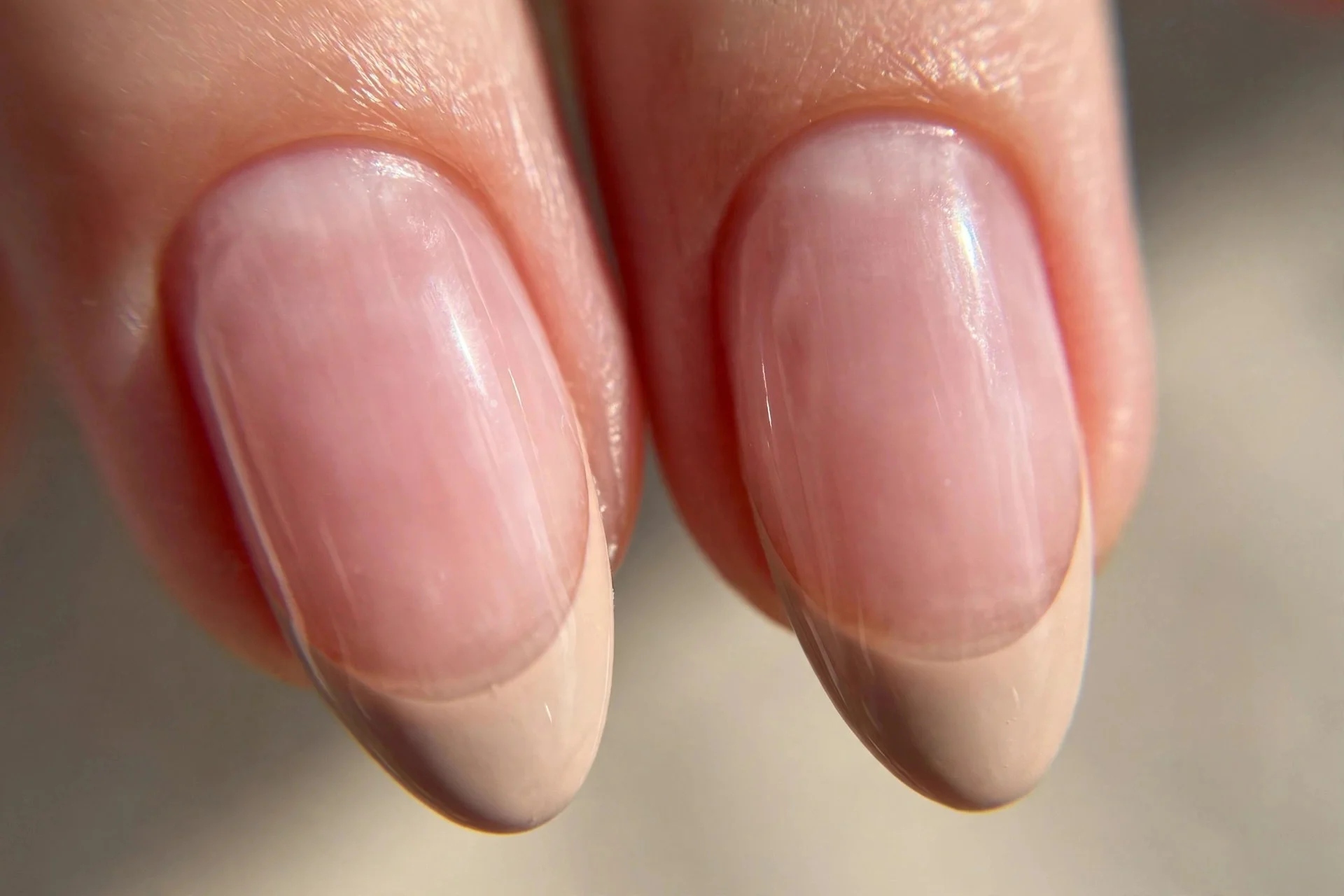 two almond fingernails with sheer pink base and soft nude beige tips