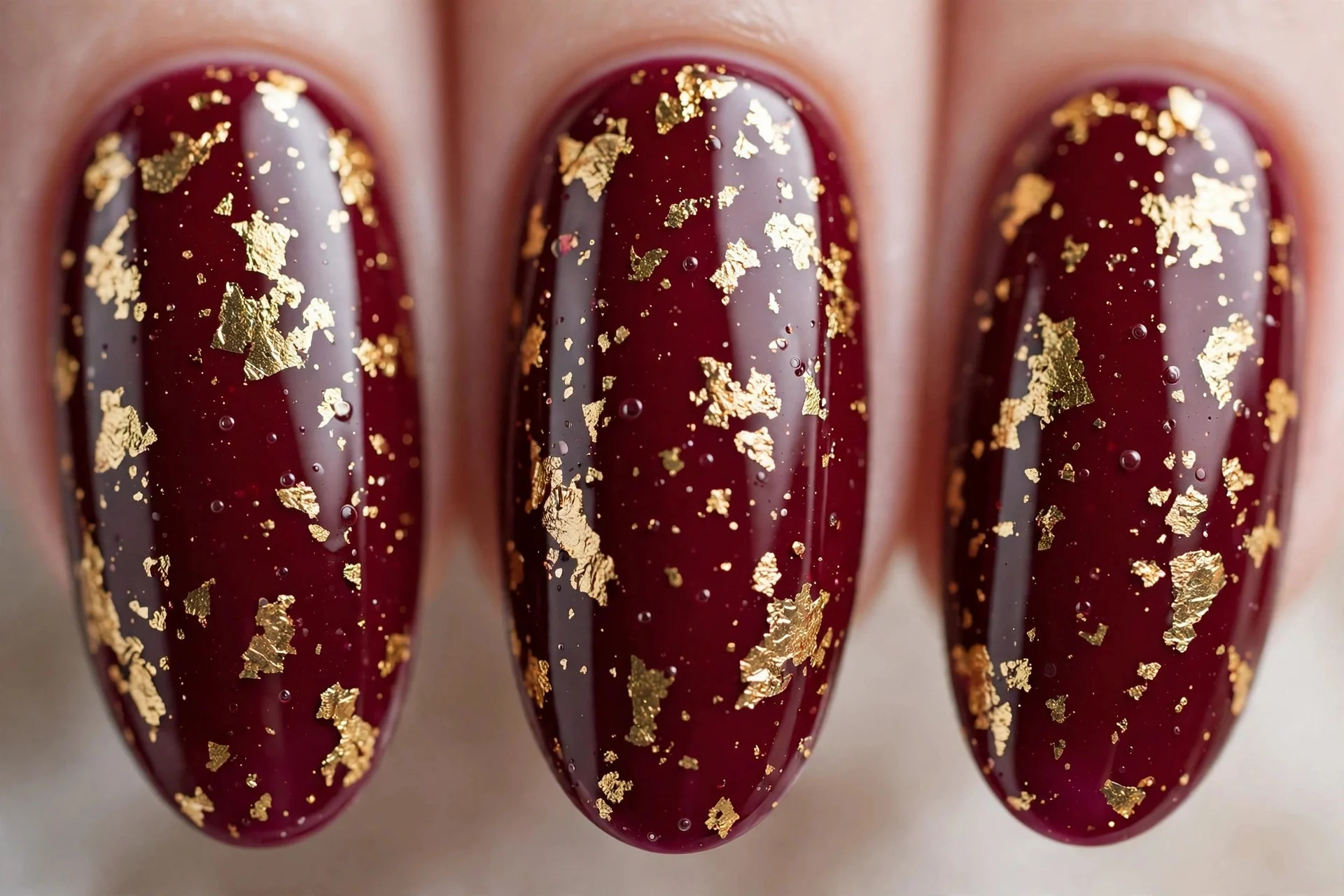 Bright claret wine polish with irregular gold foil flakes, almond nails