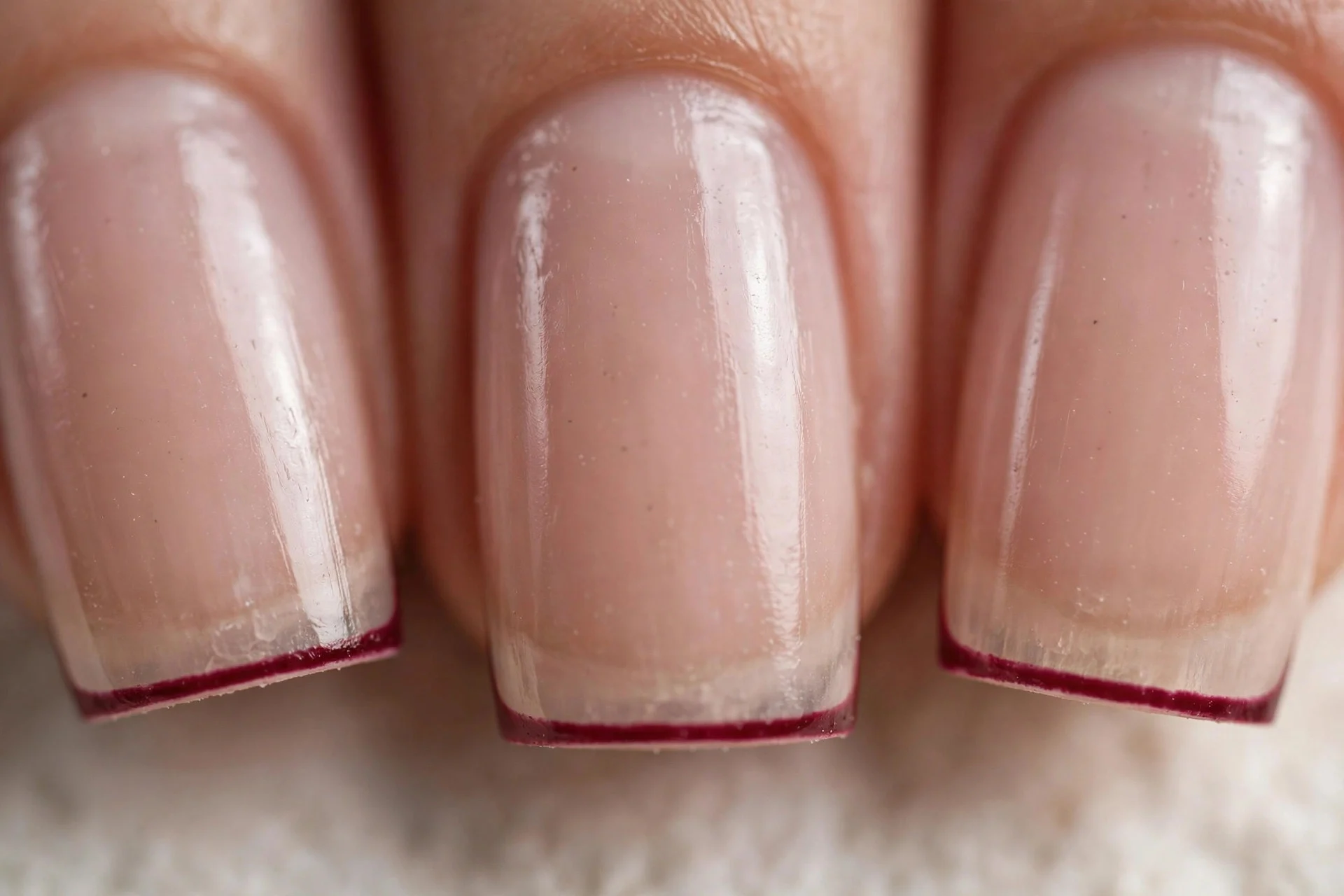 Sheer nude nails with thin wine-red micro French tips, square